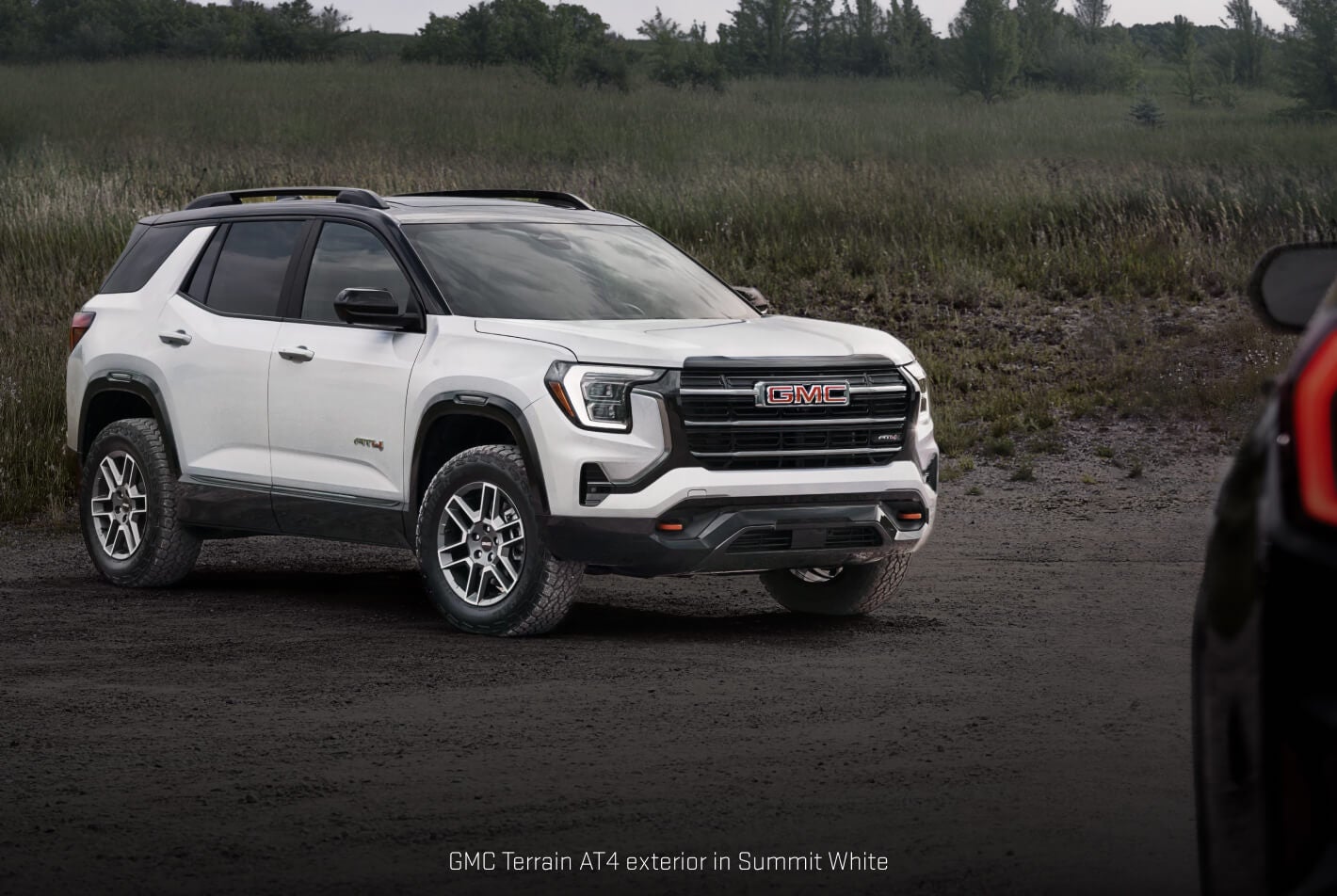GMC Terrain AT4 in Summit White showcasing its lifted ride height on a gravel trail.